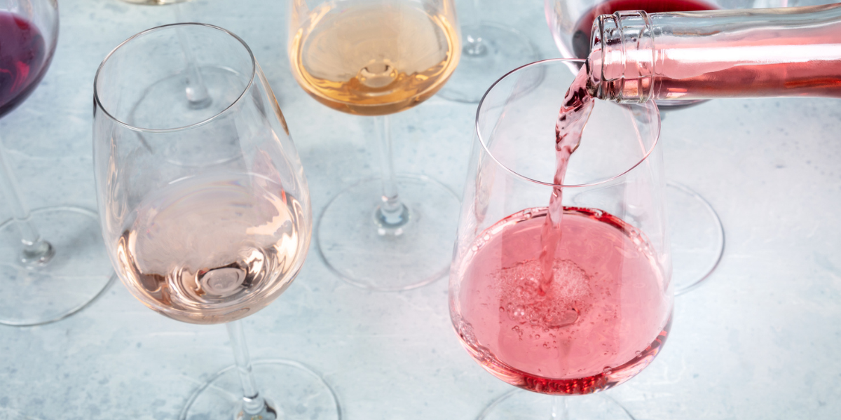 wine being poured into a glass next to other glasses of assorted wines