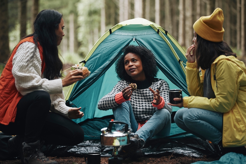 three people are seen here camping in the forest, enjoying snacks and hot drinks