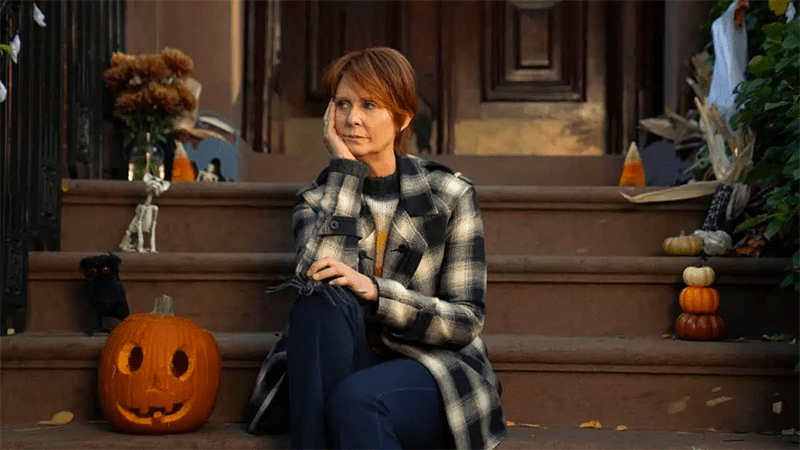 Miranda sits sadly on the porch in front of a happy pumpkin