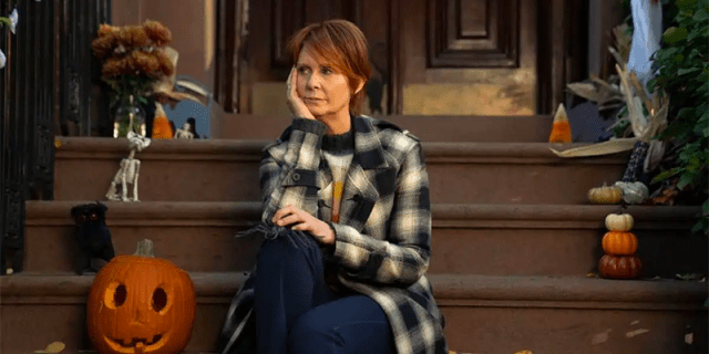 Miranda sits sadly on the porch in front of a happy pumpkin