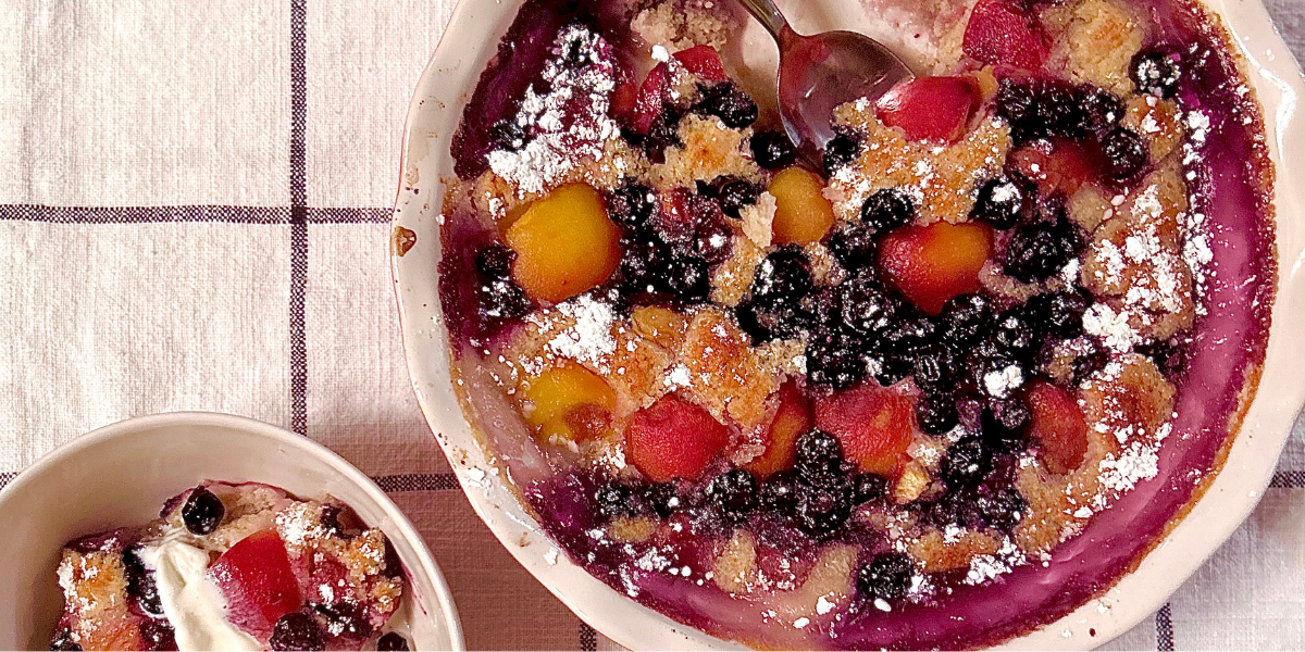 A close up image of a peach and blueberry cobbler, with this purple syrup around the edges, on a black and white checkered table cloth