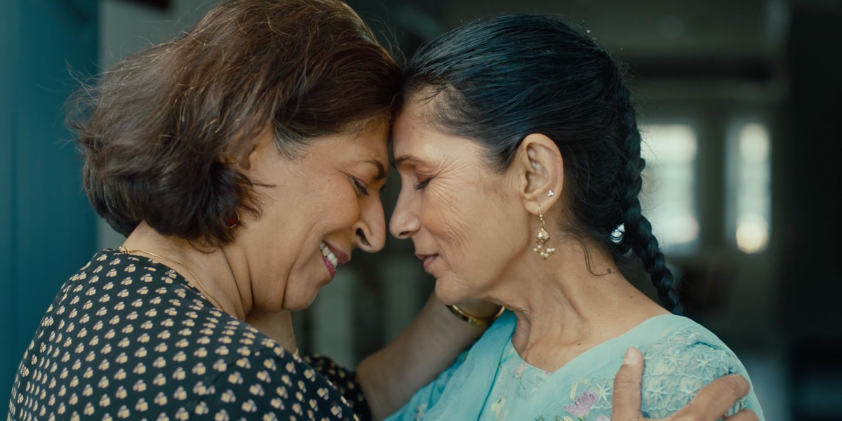 Two elder South Asian queer women touch foreheads in an intimate embrace.