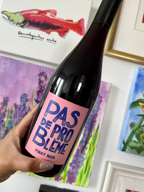 A hand holding a dark bottle of red wine against a gallery wall.