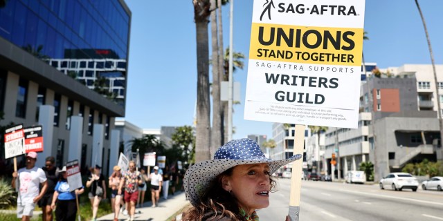 SAG-AFTRA member Christine Robert pickets in solidarity with striking WGA (Writers Guild of America) workers outside Netflix offices on July 12, 2023 in Los Angeles, California. Her sign reads: SAG-AFTRA/ Writers Guild/ Unions Stand Together