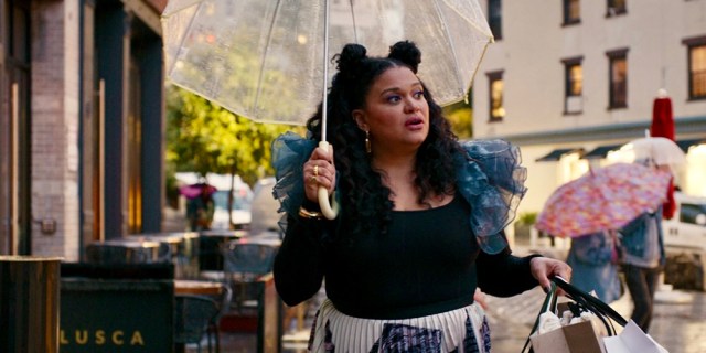 Mavis, a fat light skinned Black woman with curly hair, wears a black shirt with puffy blue sleeves and an umbrella in Survival of the Thickest.