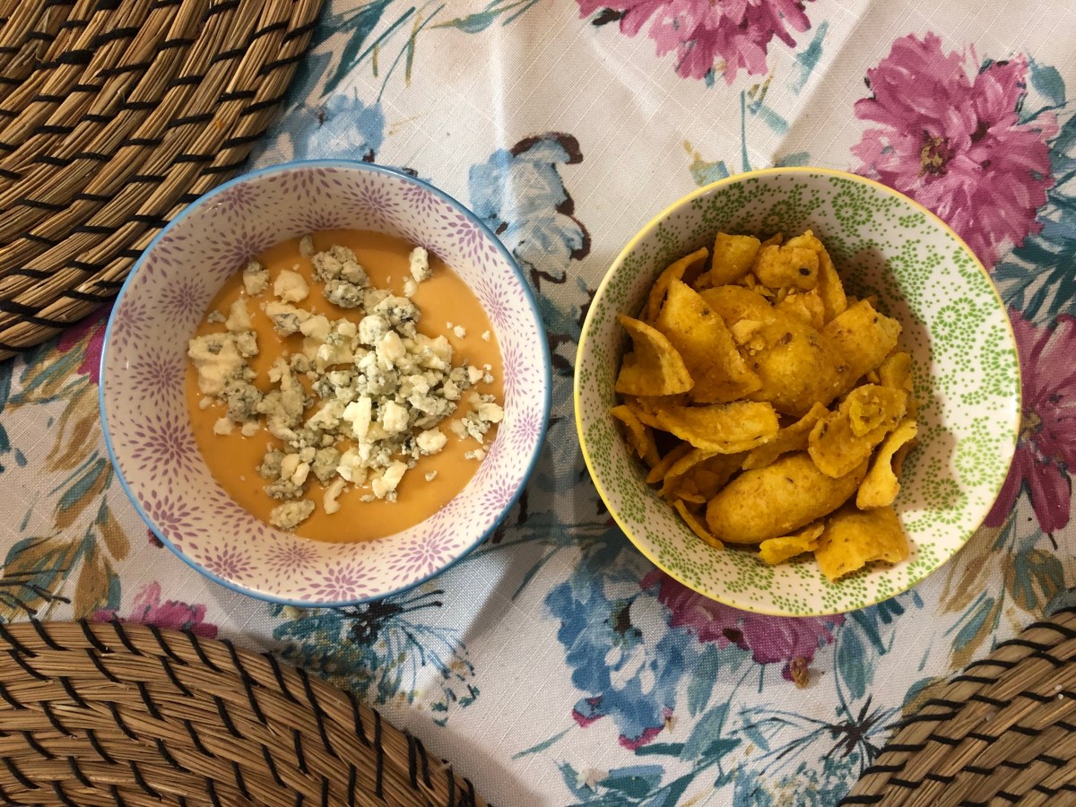 a small bowl of bean dip with bleu cheese crumbles on top and a small bowl of corn chips