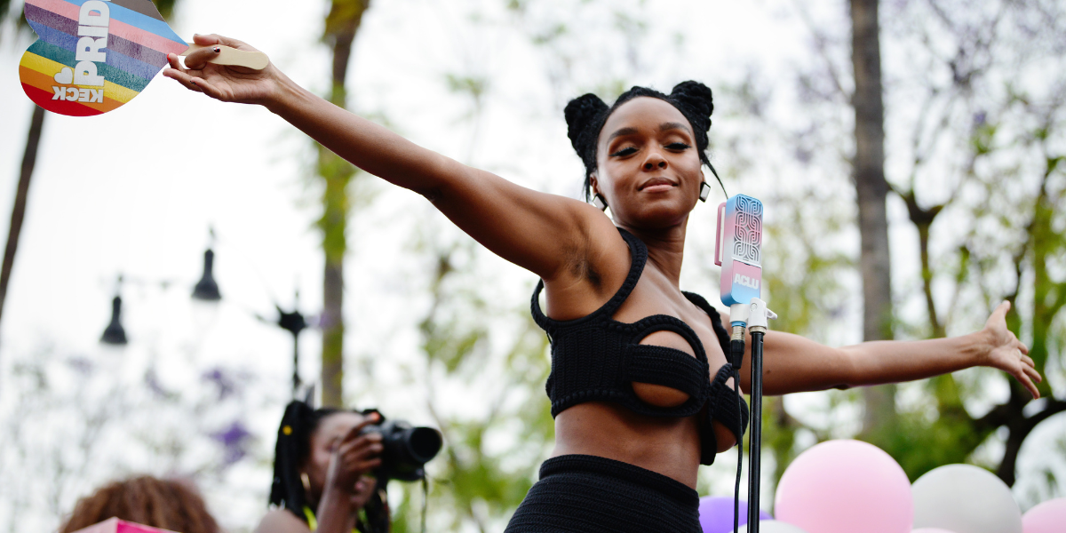Janelle Monáe holding a rainbow heart at a mic on a Pride float
