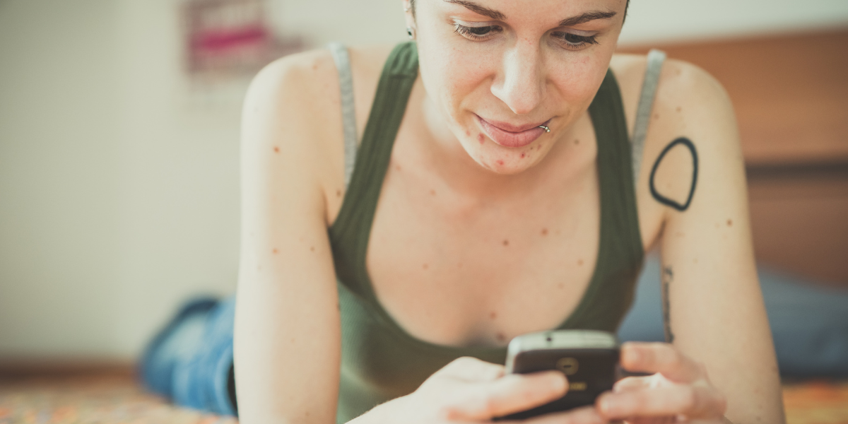 a white person with shor thair on their phone in a green tank