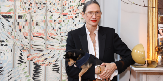 Jenna Lyons holding a dog and wearing a white buttondown and large wire frame glasses
