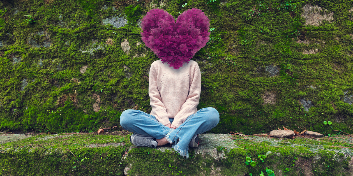 a woman sitting against a moss-covered wall outside with purple heart made of flowers over her head, with a retro collage-like effect