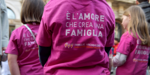 children at a protest in Italy in support of queer parental rights, wearing shirts that say "È L'AMORE CHE CREA UNA FAMIGLIA" which translates to "love creates a family"