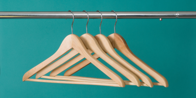 A silver closet rod with four wooden clothes hangers hanging from it. The back wall of the closet is a bright mint green.
