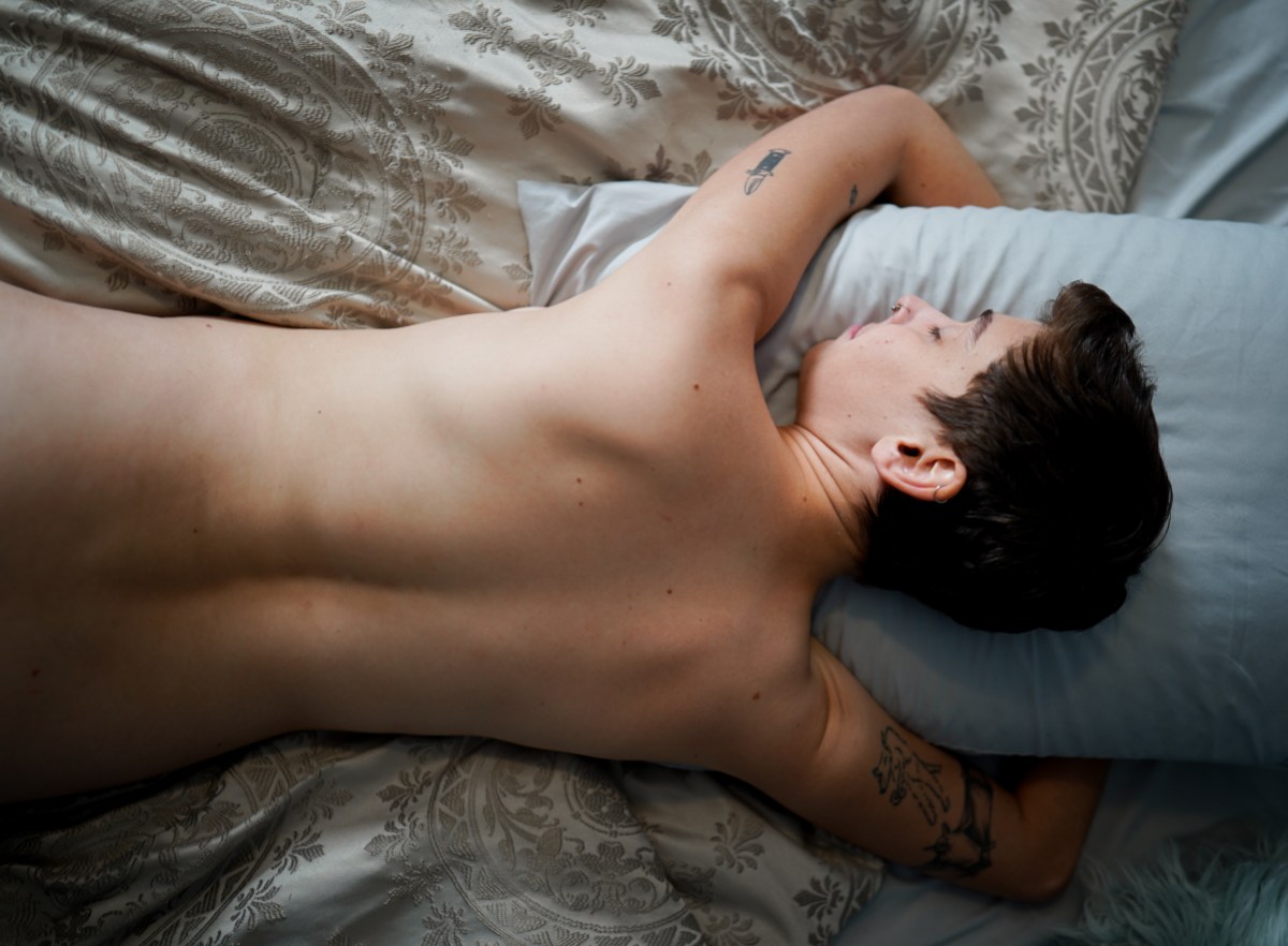 a white butch lays face down on a pillow on a bed, shirtless, peacefully slumbering