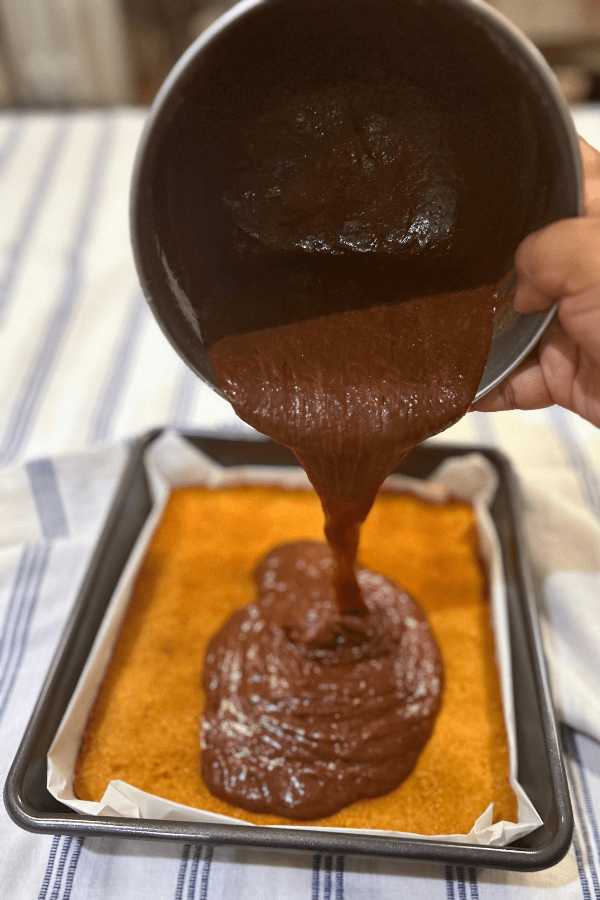 Brownie batter being poured over a graham cracker crust.