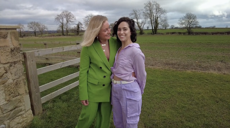 Dempsey wearing a green suit hugging Statler who is wearing a purple shirt and pants. They are standing in a field.