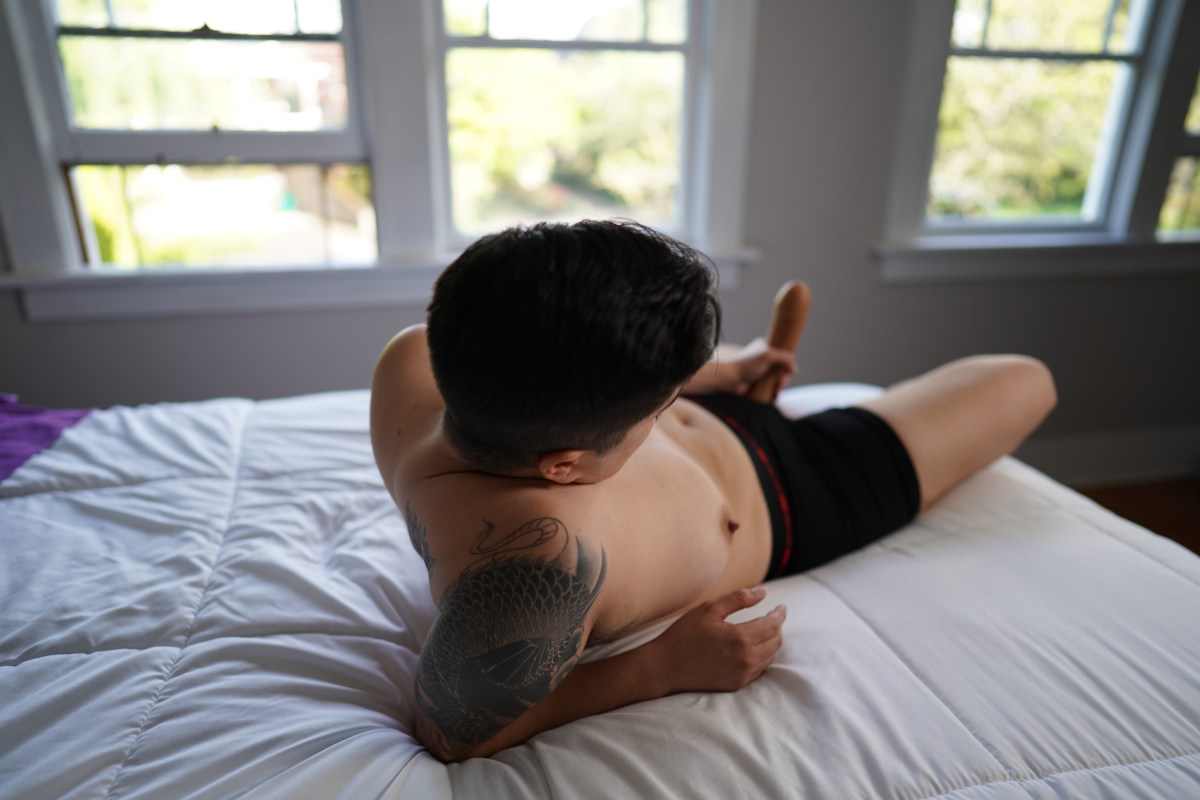 a white butch reclines topless on a bed