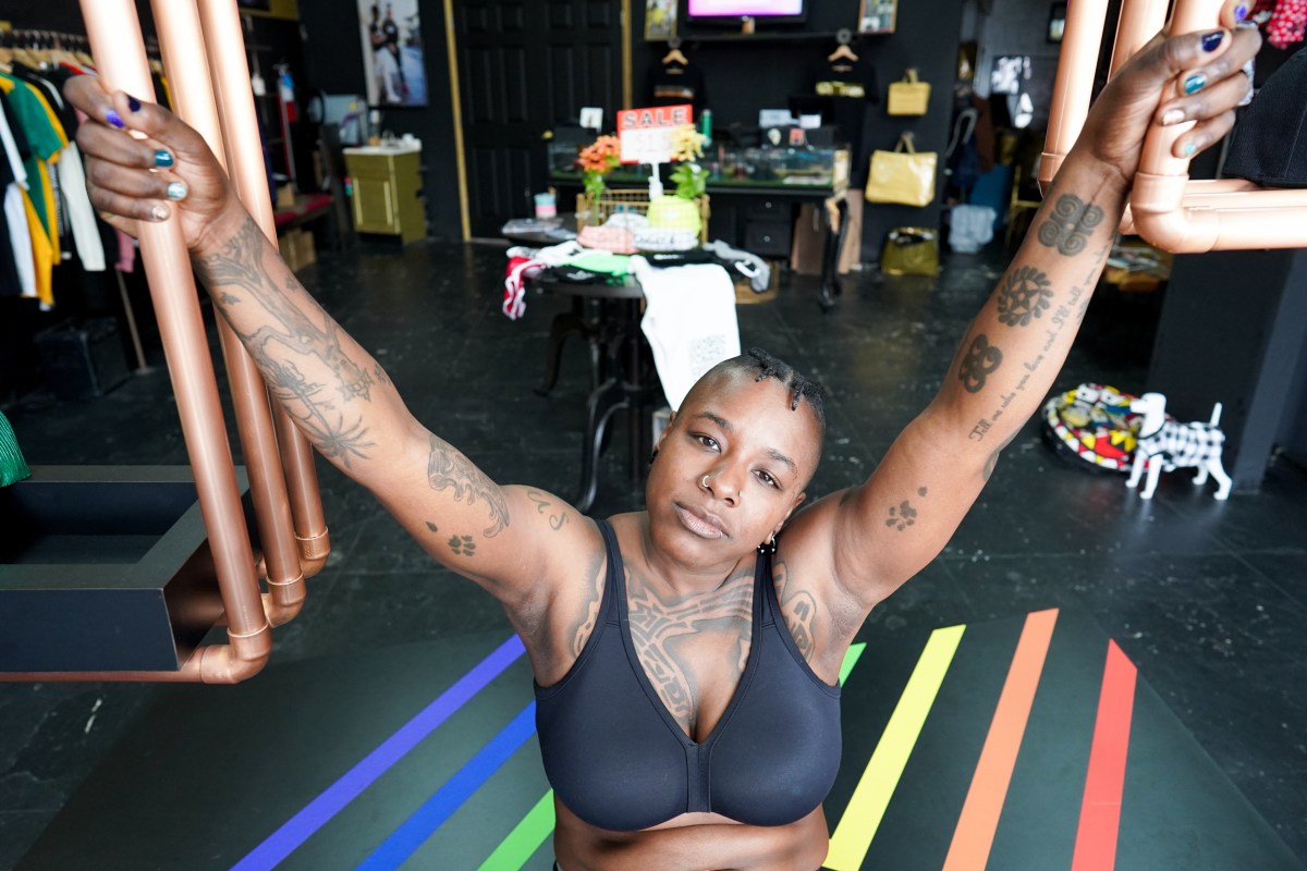 a Black stud with tattoos wears a black sports bra and has outstretched arms while looking at the camera