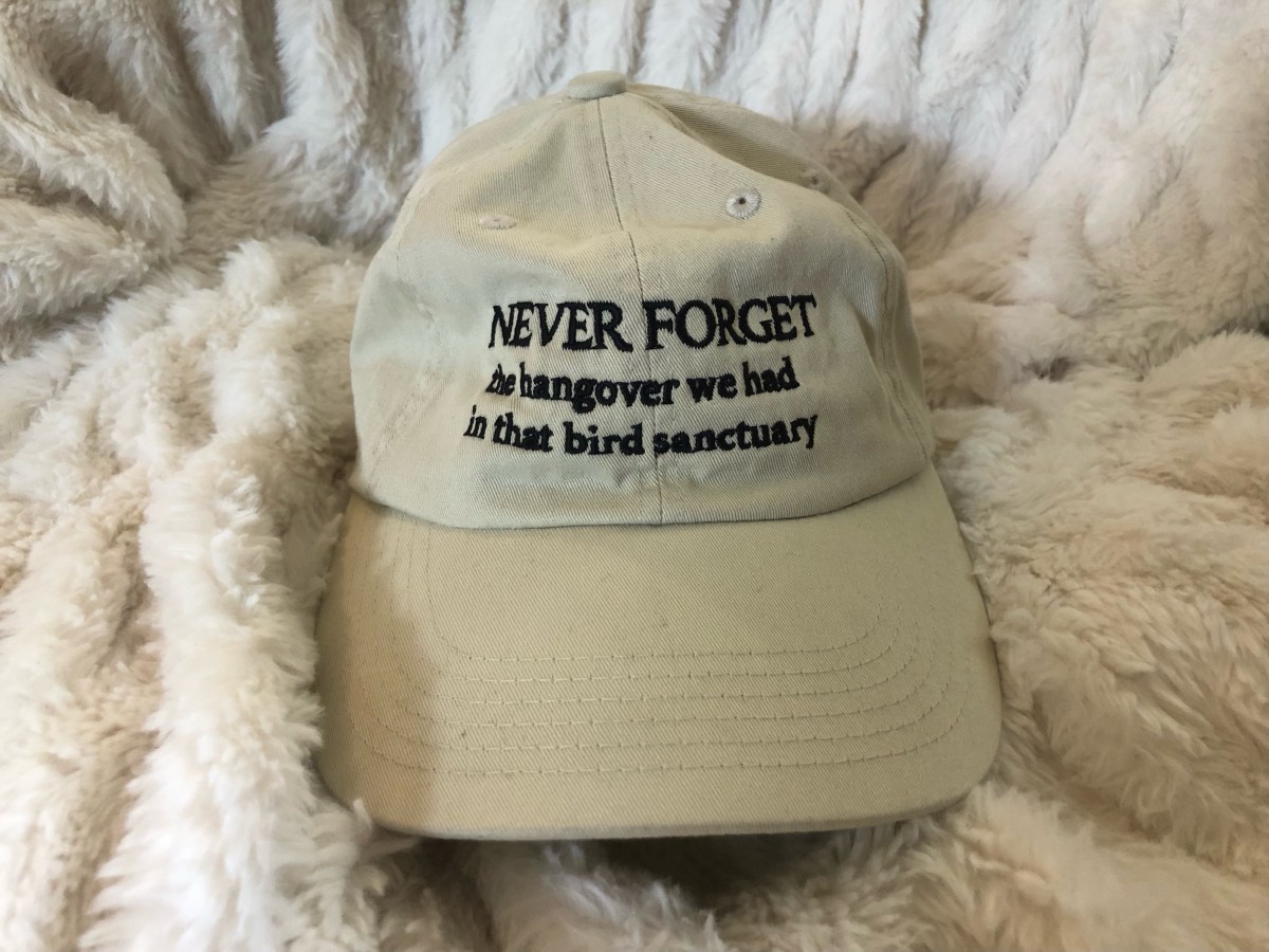 a beige hat that reads: "NEVER FORGET the hangover we had in that bird sanctuary"