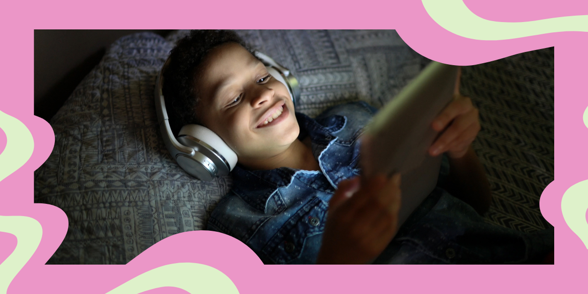 a young boy watches something on his tablet with headphones on, smiling