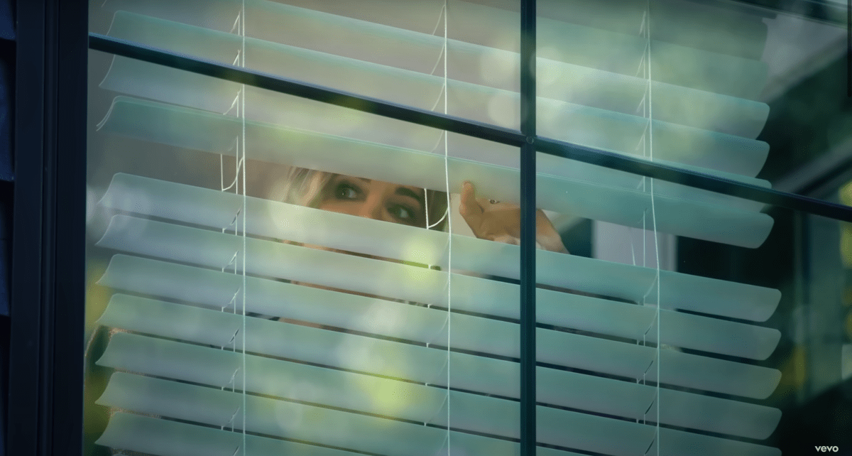 Kyle peeking out of her blinds in the Fall in Love With Me music video