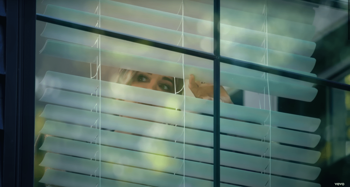 Kyle peeking out of her blinds in the Fall in Love With Me music video