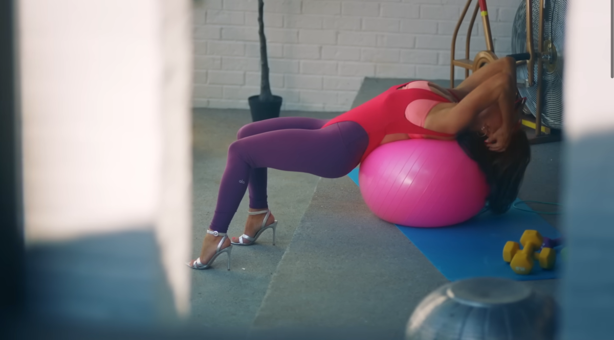 Kyle leaning back on a pink yoga ball while wearing heels and 90s garb in the Fall in Love With Me music video