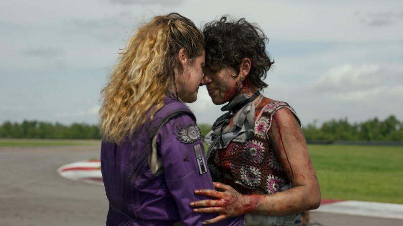 Twisted Metal: Lesbians Watts and Amber press foreheads together, covered in dirt and blood