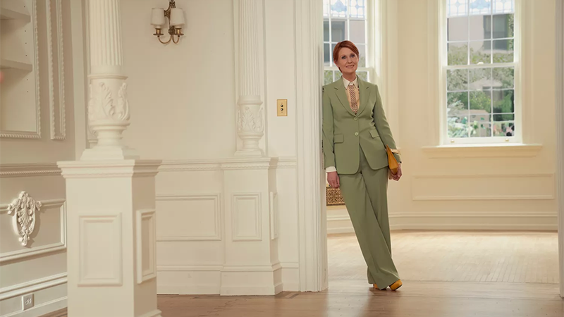 Miranda in a sea green suit, leaning against the wall. 