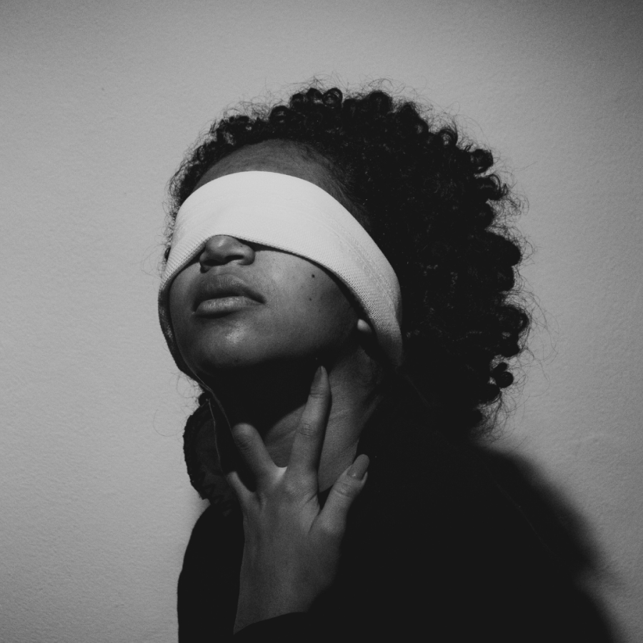 a blindfolded Black woman puts her hands to her throat in this moody photo