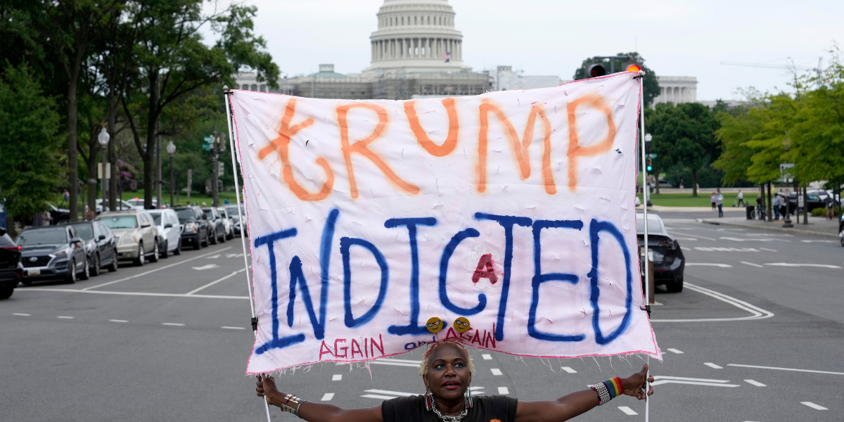 a Black woman holds up a TRUMP INDICTED AGAIN sign in front of the US Capitol