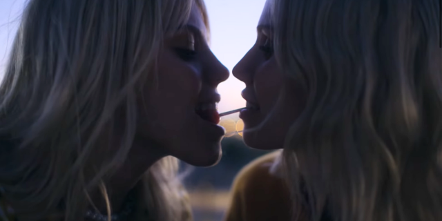 two blonde women enjoy a lollipop together