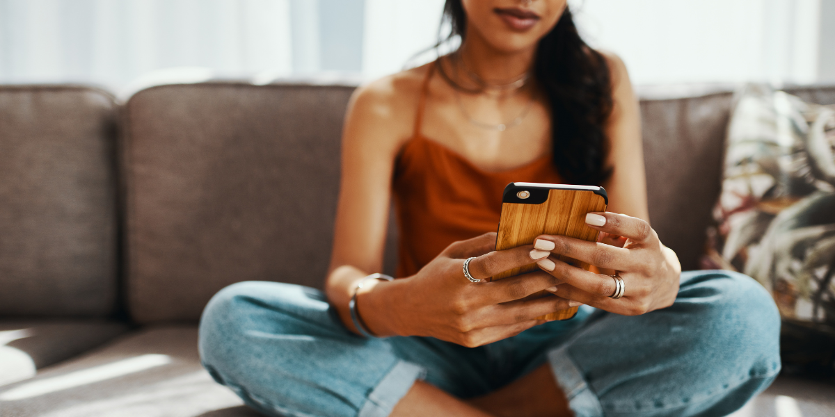 a woman sitting cross-legged on a couch looking on a dating app on her phone