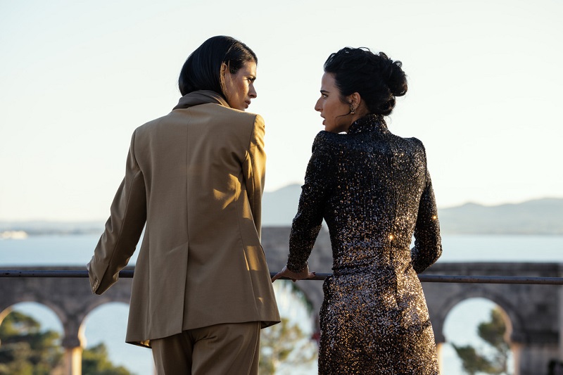 Cruz and Aaliyah engage in an intense conversation as they overlook the preparations for Aaliyah's nuptials, slated for the next day. Cruz is on the left wearing a brown pants suit, while Aaliyah is on the right, wearing a sparkly black dress.
