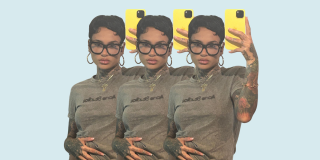 Kehlani taking a mirror selfie in a gray tee and chunky glasses