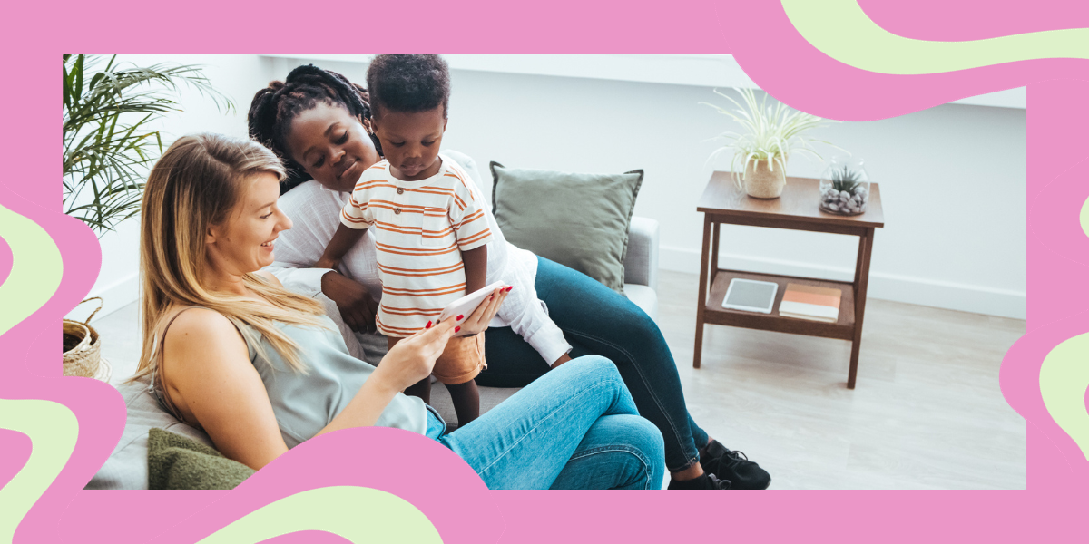 two lesbian moms with their young son on the couch, looking at something on a phone