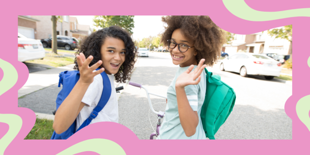 two kids with dark curly hair wave at the camera while wearing backpacks