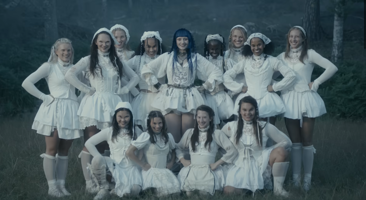 a group of terrifying looking cheerleaders in white uniforms with twisted demon faces in the woods in the music video for "Cheerleader" by Asknikko