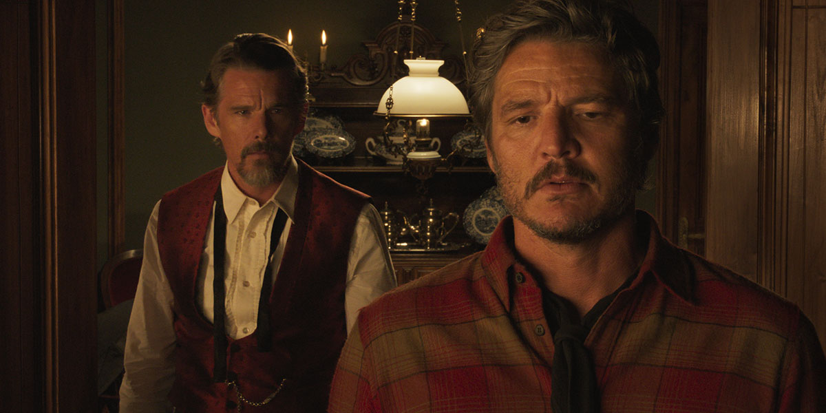Ethan Hawke stands behind Pedro Pascal dressed in Old West clothes.