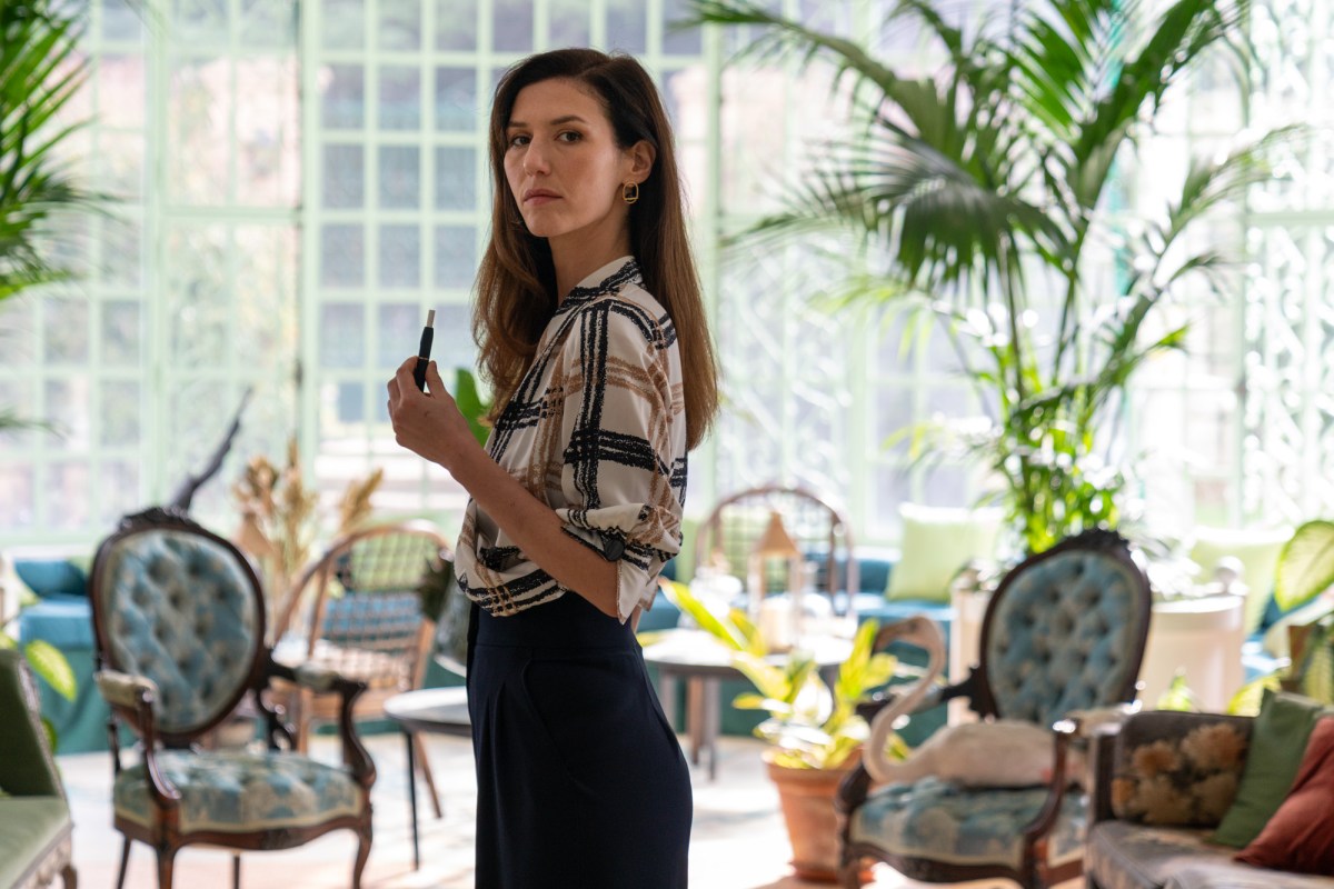 Still from The Origin of Evil. Doria Tilllier as George stands in a decadent living room holding a vape. 