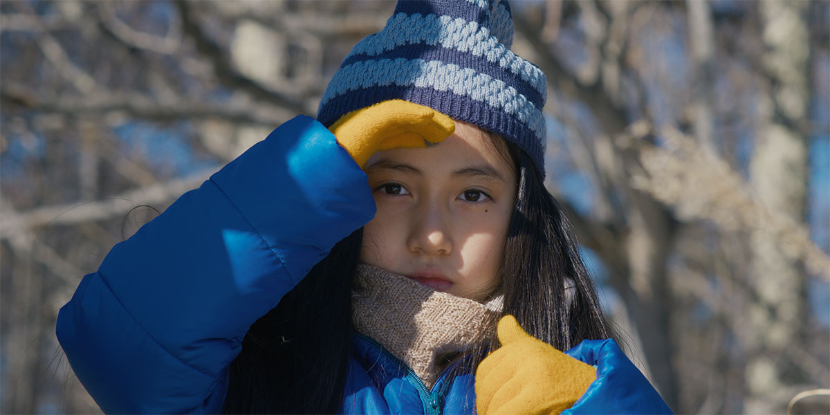 Ryo Nishikawa looks toward the camera. She is wearing a blue and yellow coat.