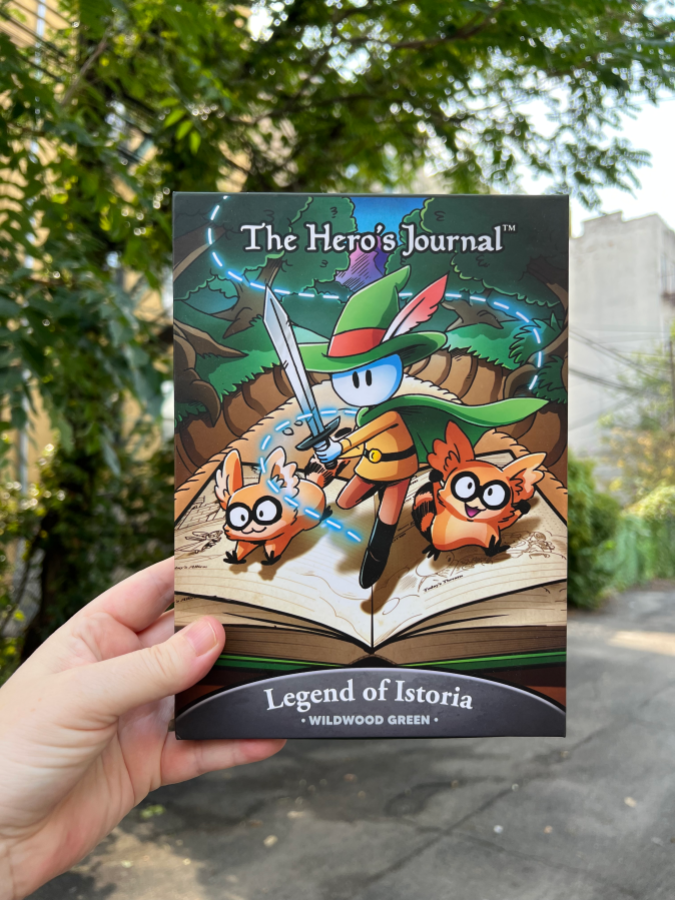 A hand holdingTHE HERO'S JOURNAL on a street in Queens, NY