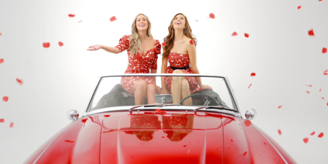 Gabby and Rachel in a promo for The Bachelorette, sitting in a red convertible throwing rose petals in the air