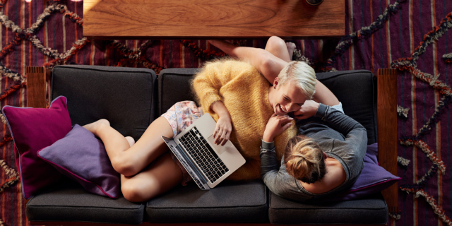 two women snuggling on a couch looking at a laptop