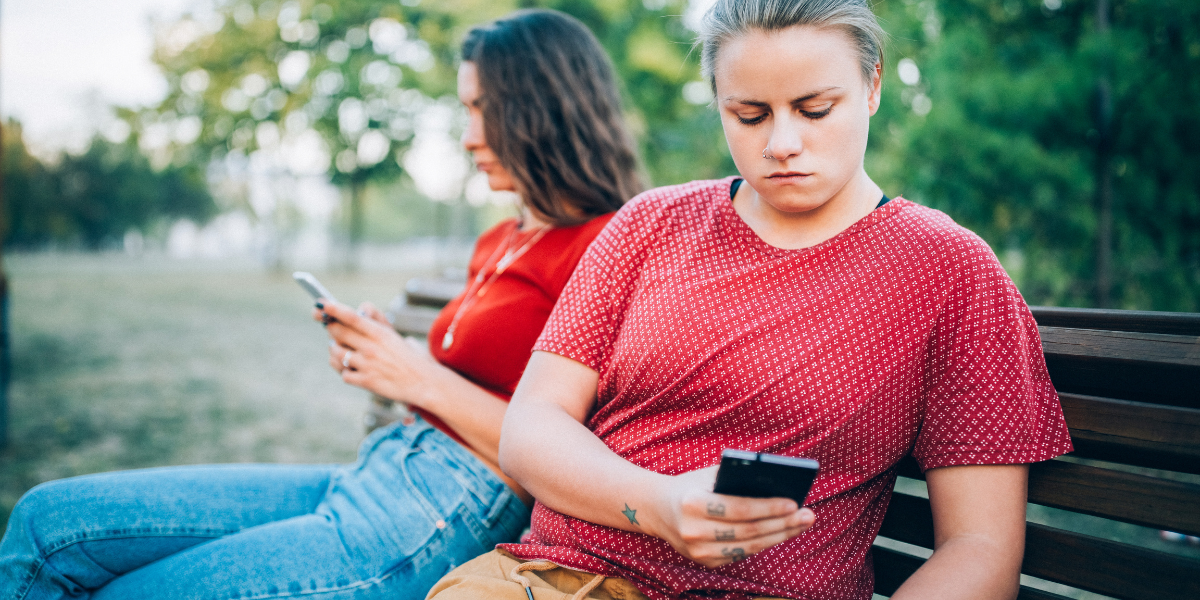 two women on their phones on a park bench