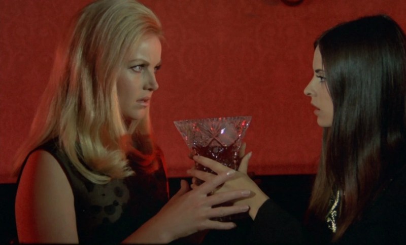 two lesbian vampires hold a glass chalice between them