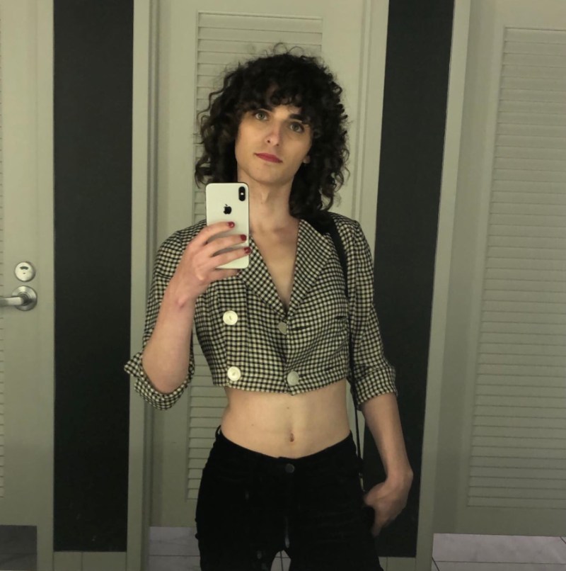 A mirror selfie of Drew from 2019. She's wearing low waisted velvet black pants and a black and white checkered crop top jacket.