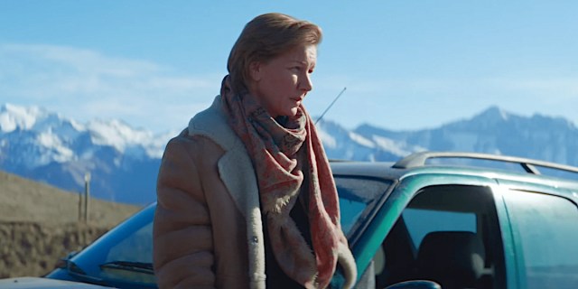 Sandra Hüller in Anatomy of a Fall. She is bundled up in warm clothes, leaning against a car, the snowy alps in the distance behind her.