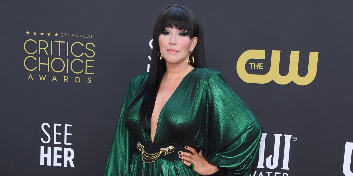 Our Lady J poses at the Critics Choice Awards in an emerald green dress with a gold belt and earrings.