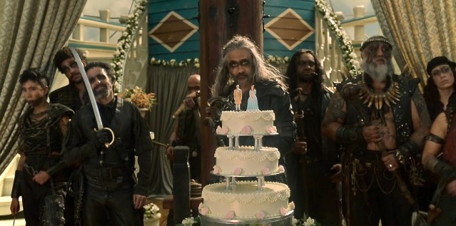 Our Flag Means Death Season Two: Black Beard stands behind a wedding cake, with a variety of other pirates behind him.