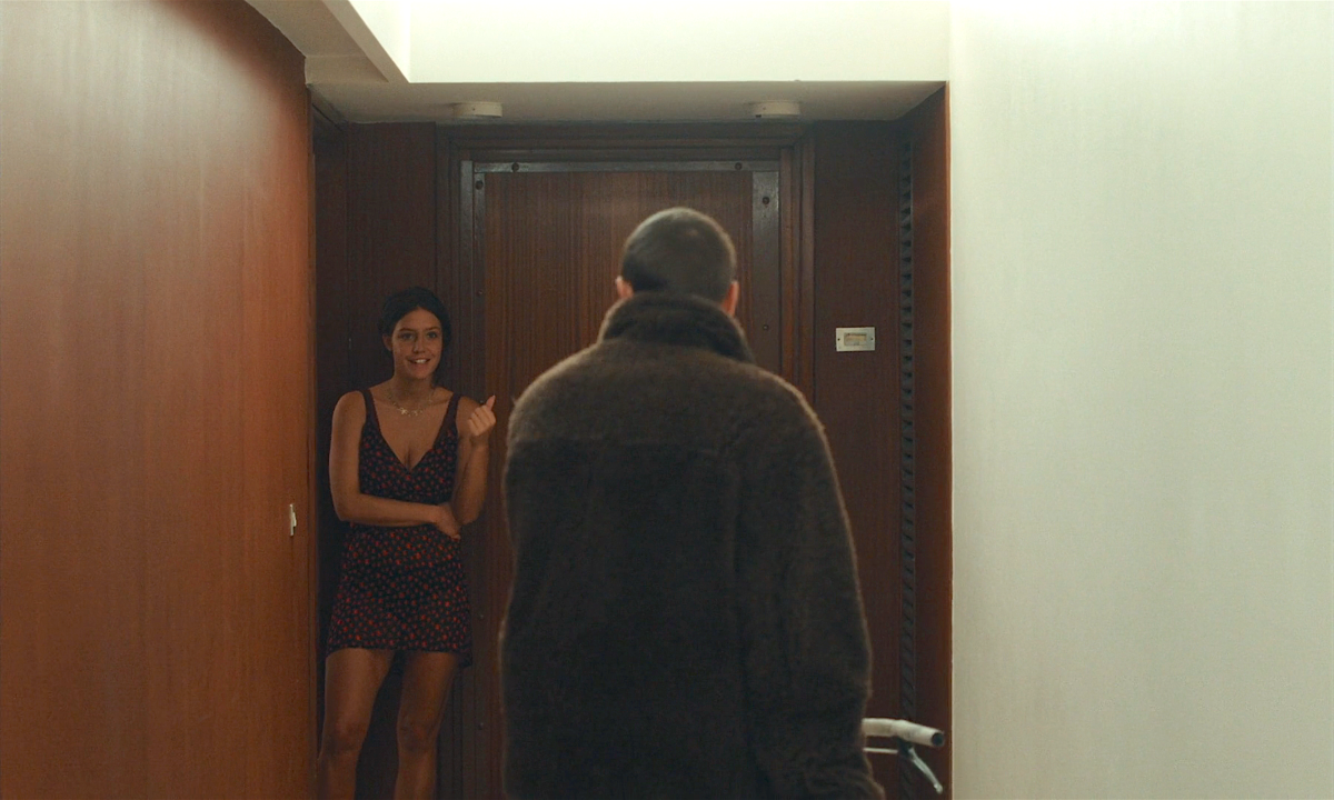 Adèle Exarchopolous wearing a black mini dress with a rose pattern stands in a hallway greeting a man.